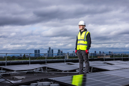 Technician standing next to solar panels on a rooftop.